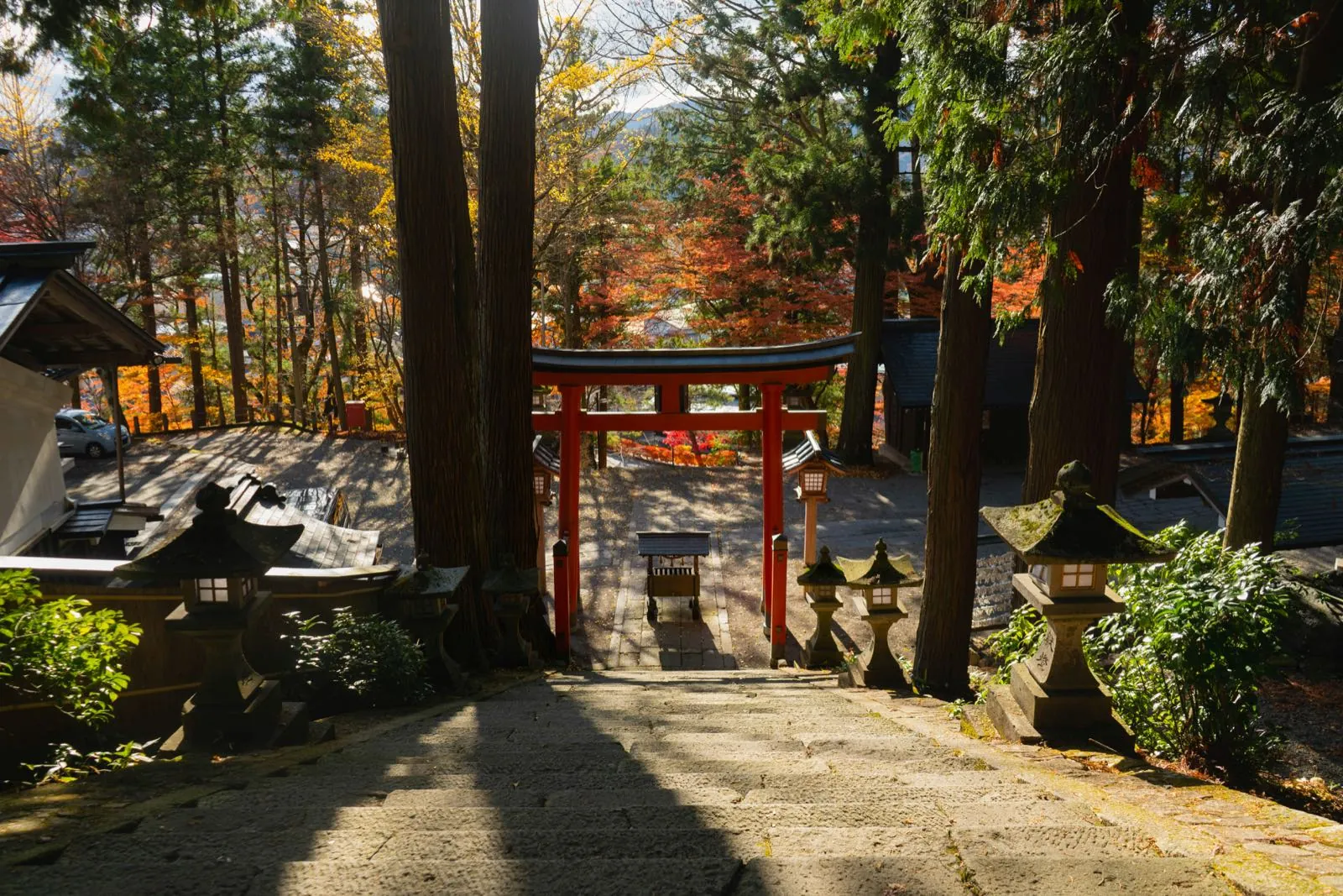 Red torii and stone staircase of a Takayama shrine among autumn maples